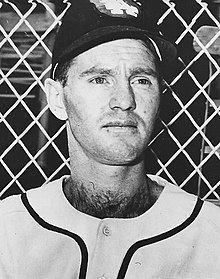 A man in a white baseball uniform and dark cap.