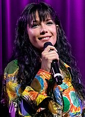 A picture of a woman dressed in multicoloured outfit singing.