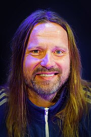 A long-haired, bearded man smiles for the camera