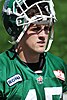 A gridiron football player wearing a green jersey with his helmet tipped back on his head