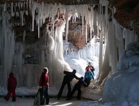 People climbing into a frozen sea cave with large icicles