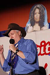 Man onstage in a Stetson hat in front of a picture of Oprah Winfrey
