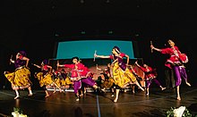 Collegiate Garba-Raas team on stage, captured during Raas section of performance (holding dandiyas) dressed in traditional attire