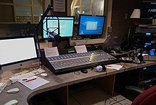 Inside the WQSU broadcasting room, where the on-air DJ's play their music and programs. There is a hanging microphone and three computers on the left that holds the music library where all the music is stored. There is also a clock to the right to indicate the time and keep the DJs on schedule, and a dashboard to control the levels of sound during the shows.