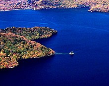 Photo couleur d'un îlot dans une étendue d'eau couleur bleu de cobalt. La rive boisée du lac en arrière-plan.