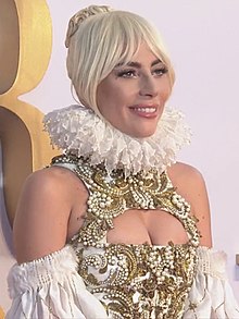 Lady Gaga smiling and wearing a golden outfit.