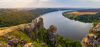 Vista panorâmica das colinas que dominam o rio Dniestre perto da aldeia de Nahoriany, região de Tchernivtsi, Ucrânia. O Dniester é um rio do Leste Europeu. Ele nasce na Ucrânia, perto da cidade de Drohobych, na fronteira com a Polônia, e flui em direção ao mar Negro. Seu curso marca parte da fronteira da Ucrânia e da Moldávia, após o qual flui através da Moldávia por 398 quilômetros, separando o principal território da Moldávia de sua região separatista, a Transnístria. Mais tarde, forma uma parte adicional da fronteira Moldávia-Ucrânia, então flui através da Ucrânia para o mar Negro, onde seu estuário forma o Liman do Dniester. Ao longo da metade inferior do rio, a margem oeste é alta e montanhosa, enquanto a leste é baixa e plana. Durante o Neolítico, o rio foi o centro de uma das civilizações mais avançadas da Terra na época. A cultura Cucuteni-Tripiliana floresceu nesta área de cerca de 5300 a 2600 a.C., deixando para trás milhares de sítios arqueológicos. Seus assentamentos tinham até 15 mil habitantes, tornando-os uma das primeiras grandes comunidades agrícolas do mundo. (definição 7 087 × 3 376)