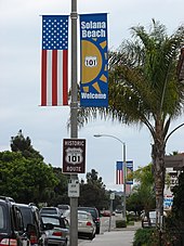 View from a sidewalk of several banners and signs with the U.S. 101 shield displayed in decorative fashion alongside an American flag pattern.