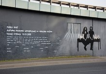 A stark black, white, and gray mural depicting two members of the group sitting on a bench with prison bars in the background.