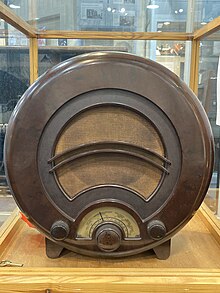 A round dark brown Bakelite radio in a display stand.