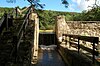 Water pours over a narrow spillway with a sunlit stone dam structure on either side