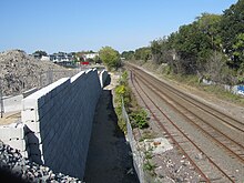 A below-grade railroad corridor, with a retaining wall and construction site at left
