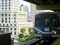 A Metrorail train is approaching the upper level of the Government Center station with the Dade County Courthouse in the background.