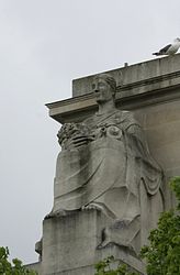 Stone statue of a seated woman holding flowers and an animal's skull on her lap