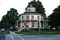 Large timber frame house, pitched roof and lantern, veranda all round. Arched windows and window shutters add to the decorative effect. The Rich-Twinn Octagon House in Akron, New York.