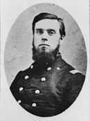 Black and white photograph shows a dark-haired young man with a beard, but no moustache. He wears a dark uniform with two rows of buttons.