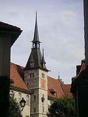 Photo en couleur d'un bâtiment avec toit rouge pentu, tourelle et clocheton, sur fond de ciel bleu.