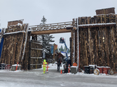 A tall wooden gate covered in snow, with a traffic controller in the midground and a crane with crew members in the background.