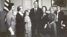 President Lyndon B. Johnson poses in the Oval Office with six white women, all winners of the 1964 Federal Woman's Award; from left to right: Elizabeth Messer, Evelyn Anderson, Gertrude Blanch, President Johnson, Patricia van Delden, Margaret Schwartz, and Selene Gifford