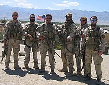 A color image of six military personnel dressed in their combat uniforms and holding weapons.