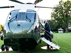 Donald Trump, wearing a black face mask, boards Marine One, a large green helicopter, from the White House lawn