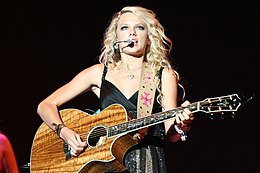 Taylor Swift singing on a microphone and playing a guitar