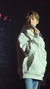 Photograph of B.I standing with a microphone in his hand