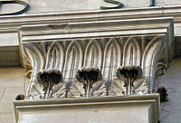 A square carved stone capital with two different types of leaves going up and around to the top