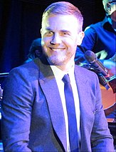 A Caucasian man, wearing a suit is smiling