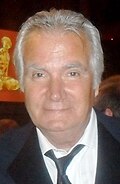 A man with grey hair, wearing a black a suit.