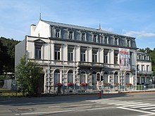 Bâtiment de style néoclassique à la façade en pierre et enduit comprenant neuf baies sur deux niveaux surplombés d'un étage mansardé en ardoises à sept fenêtres