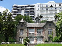 Photographie en couleurs d'une villa dont la toiture porte un clocheton central ; immeuble moderne en arrière-plan.