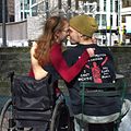 A woman in a wheelchair embracing a man in a chair