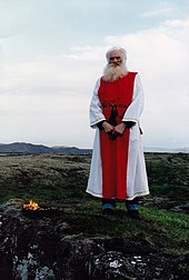 An elderly man wearing red and white robes standing in an open area