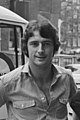 Black and white photo of young white man with dark wavy hair wearing an open-necked shirt