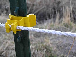 Detail of electric cord fence with metal interwoven with nylon cord, attached to a steel fence post with a plastic insulator