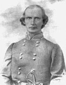 Black and white photo shows a clean-shaven man with a receding hairline. He wears a gray military uniform with two rows of buttons.