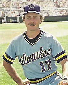 A man in a powder blue baseball jersey with "Milwaukee" written across the chest and a blue cap kneeling on a baseball field