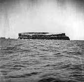 Photo en noir et blanc prise depuis un bateau avec la mer et au centre le rocher