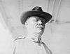 Man facing slightly right in uniform with hat and gasses without temple bridges