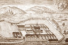 Engraving showing a Carthusian monastery situated at the foot of hills and surrounded by a wall.
