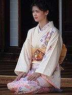 A young woman kneeling in an offwhite formal kimono with a traditionally-stylized pink blossom pattern