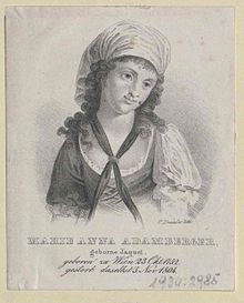 Black and white image depicting the upper body of a young woman. She is wearing a simple dress resembling a folk costume with a white chemise under a dark bustier. There is a narrow black scarf on her neck, forming an X-shape on her bust, and she is wearing simple white headcovering. Her hair is dark and curly. An inscription in German states that this is "Marie Anna Adamberger, geborne Jaquel. [G]eboren zu Wien 23 Okt. 1752. [G]etorb. daselbst 3. Nov. 1804."
