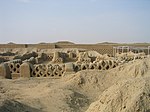 Ruins of former buildings in a desert setting consisting of low walls with a fishnet pattern.