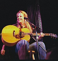 Singer Mary Chapin Carpenter, seated while holding a guitar.
