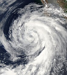 A photograph of a tropical storm off the Pacific coast of Mexico. Most of the thicker clouds are on the right side of the storm, particularly in a long curved band that arcs to the south.