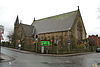 A small stone church with a transept and an octagonal bell turret with a conical roof