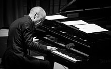 A black-and-white photo of a man playing a piano; he is hunched over it and is concentrating deeply.