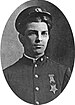 Head and shoulders of a young white man wearing a cap pushed high up on his forehead and a plain military jacket with a star–shaped medal hanging from a ribbon pinned to his left breast.