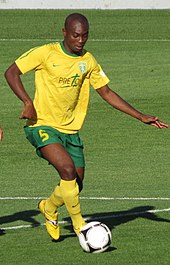 Un joueur de football en maillot jaune, ballon au pied, sur un terrain de football.